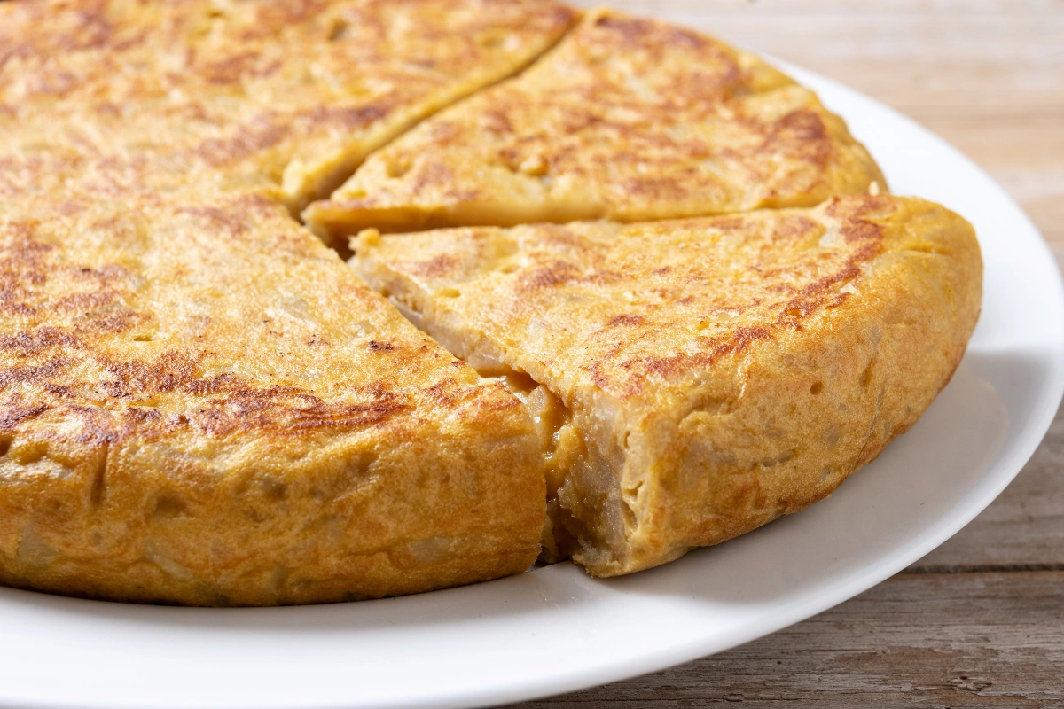 A golden, whole vegan cornbread on a white plate with a slice partially removed, showcasing its moist and fluffy texture.