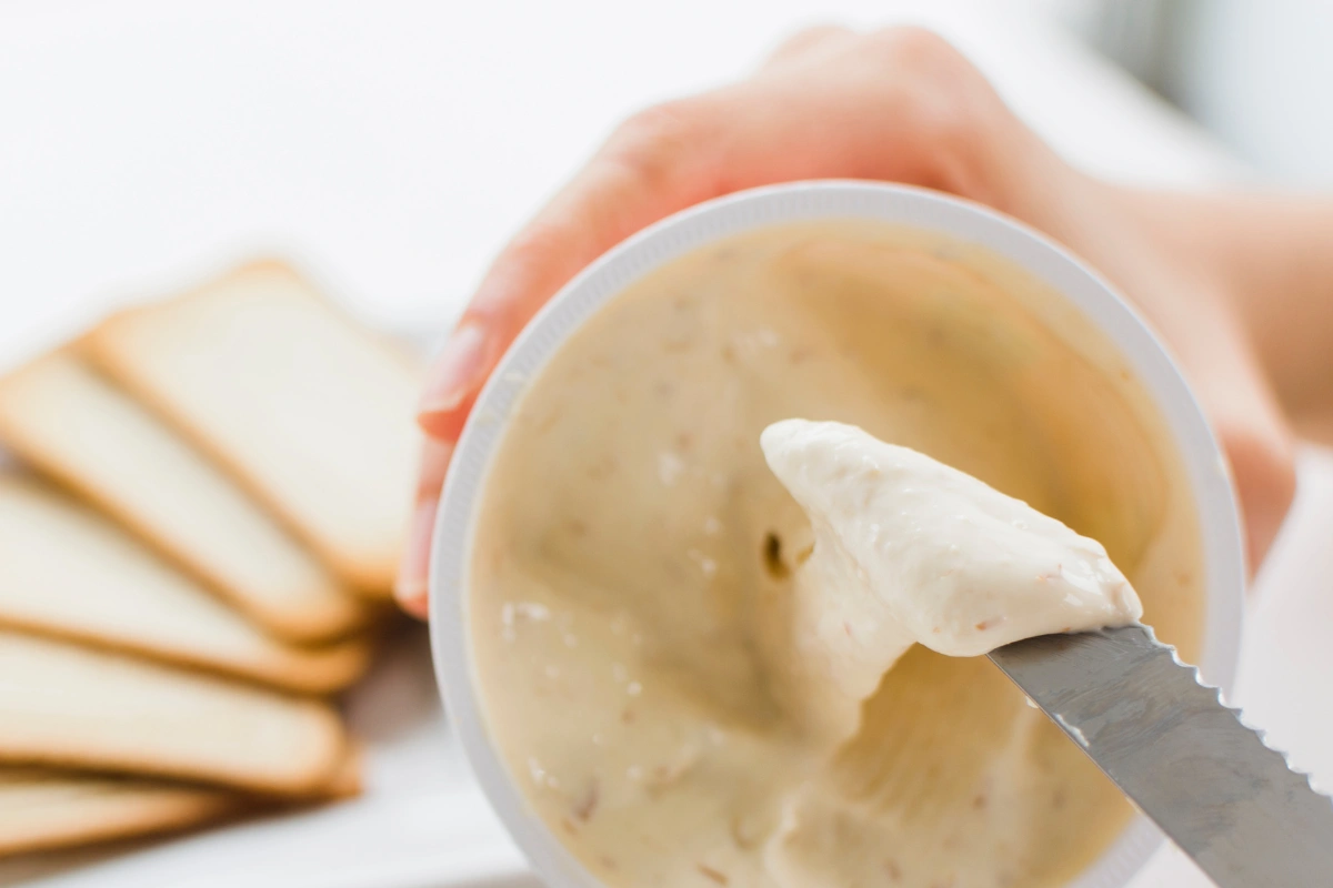 Spreading creamy vegan cream cheese onto bread with a knife.