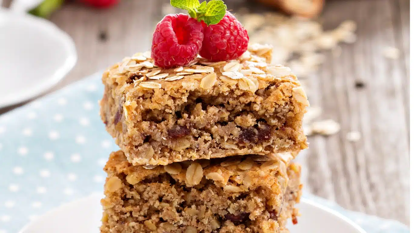 A flat-lay of ingredients for a vegan flapjack recipe, including oats, maple syrup, bananas, and coconut oil on a rustic wooden surface.