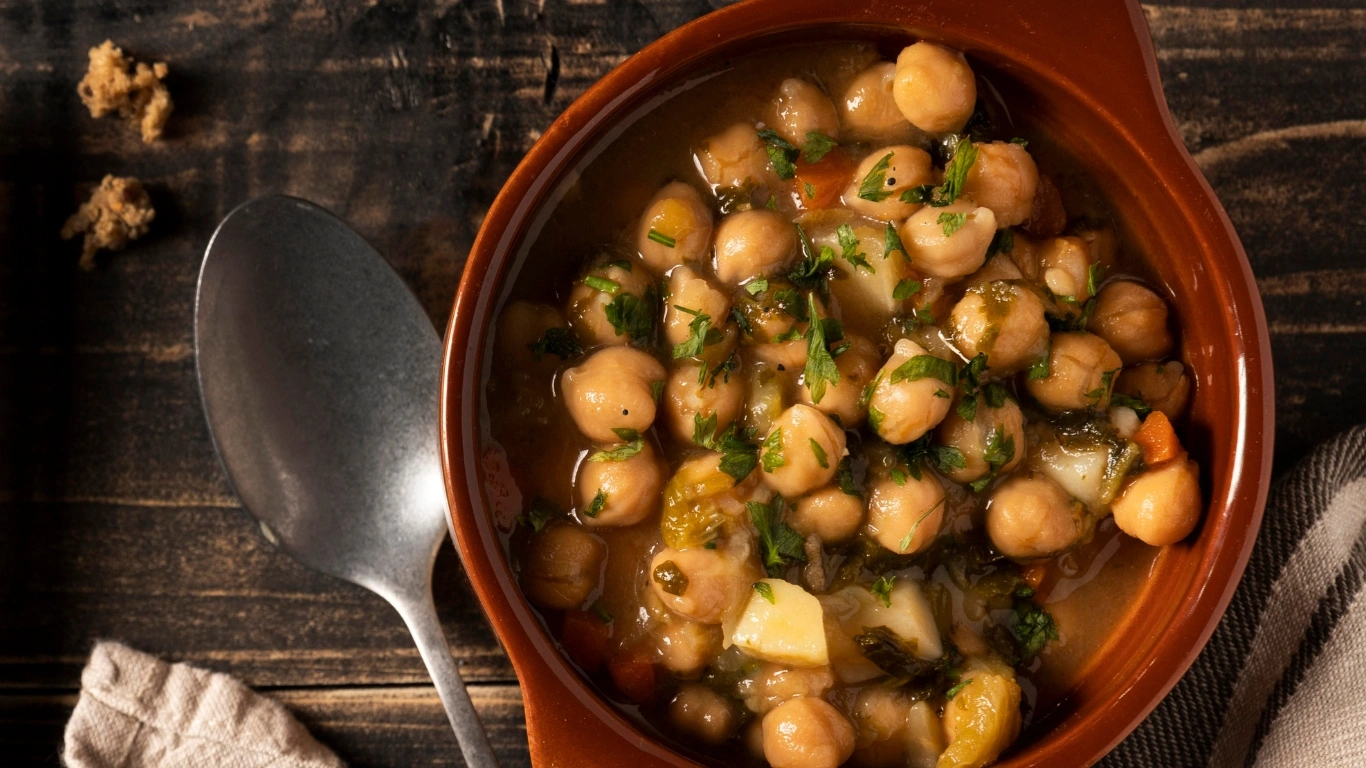 Vegan crock pot recipe featuring chickpea stew in a brown bowl, garnished with parsley on a rustic wooden table.
